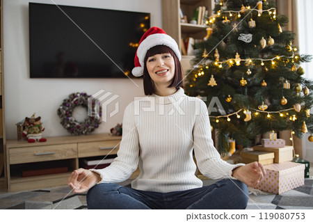 Young woman meditating in front of Christmas tree at home 119080753