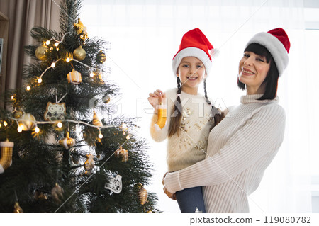 Mother and daughter celebrating Christmas by decorated tree 119080782