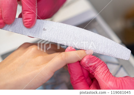 Nail technician carefully files a clients nails during a manicure session in a salon Nail technician carefully files a clients nails during a manicure session in a salon 119081045