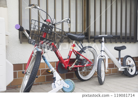 Children's bicycles, striders and kick scooters parked in front of a house Children's bicycles, striders and kick scooters parked in front of a house 119081714