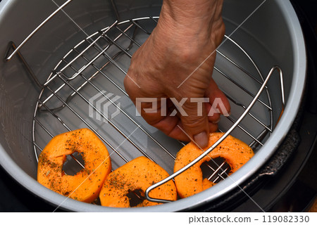 A woman's hand places a pumpkin in a multicooker. Close-up. 119082330
