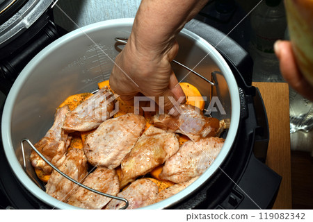 A woman's hand places meat in a multicooker. 119082342