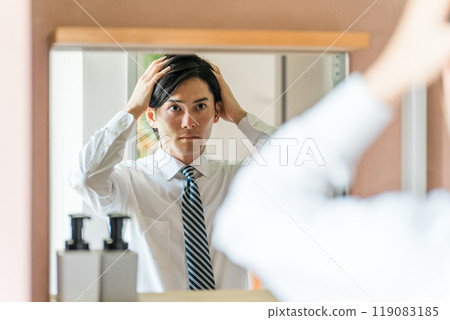A young Asian male businessman in a suit styling his hair before going to work in the morning 119083185