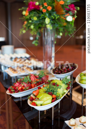 Variety of fruits, featuring vibrant fruits like strawberries, watermelon, and grapes, along with a vase of orange and green flowers, ready for a celebration. 119083735