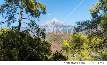 Tahtali Olympos mountain peak as seen from the Lycian Way in Cirali, Antalya, Turkey. The scenic landscape features lush forests, blue skies, and rugged slopes. 119083751