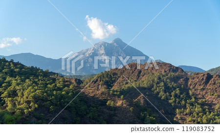 Tahtali Olympos mountain peak as seen from the Lycian Way in Cirali, Antalya, Turkey. The scenic landscape features lush forests, blue skies, and rugged slopes. 119083752