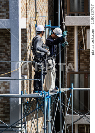 A scaffolder erecting scaffolding at a large-scale repair work site for an apartment building, with safety as the first priority A scaffolder erecting scaffolding at a large-scale repair work site for an apartment building, with safety as the first priority 119083797