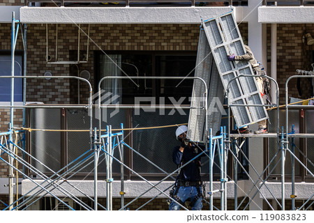 A scaffolder erecting scaffolding at a large-scale repair work site for an apartment building, with safety as the first priority A scaffolder erecting scaffolding at a large-scale repair work site for an apartment building, with safety as the first priority 119083823