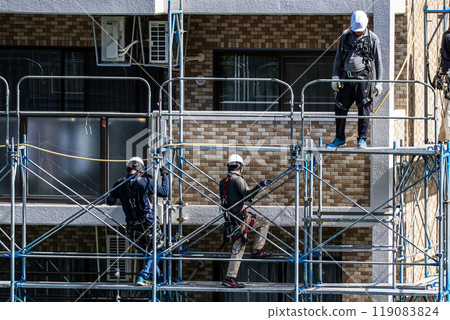 A scaffolder erecting scaffolding at a large-scale repair work site for an apartment building, with safety as the first priority A scaffolder erecting scaffolding at a large-scale repair work site for an apartment building, with safety as the first priority 119083824