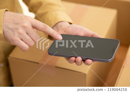 一名中年婦女帶著智慧型手機和用紙板包裝的行動行李 一名中年婦女帶著智慧型手機和用紙板包裝的行動行李 119084258