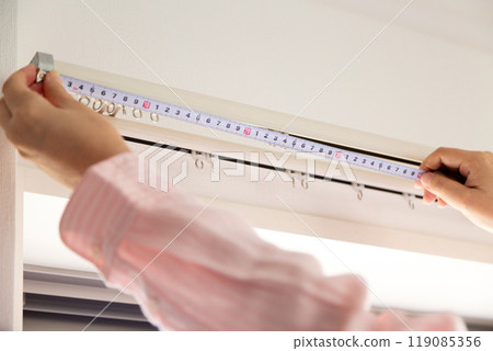 一位中年婦女在公寓窗戶邊測量窗簾的尺寸。 119085356