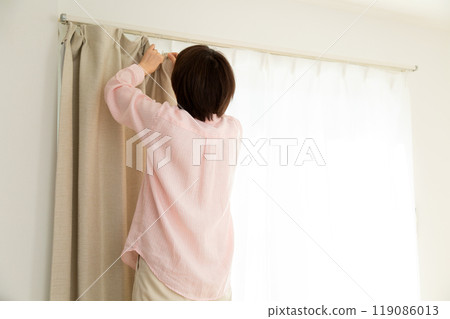 A middle-aged woman installing curtains in an apartment 119086013