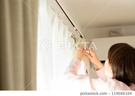 A middle-aged woman installing curtains in an apartment A middle-aged woman installing curtains in an apartment 119086104