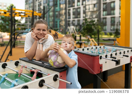 A joyful moment shared between a mother and son at a city playground, enjoying foosball and soccer A joyful moment shared between a mother and son at a city playground, enjoying foosball and soccer 119086378