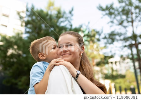 A joyful moment between a mother and son sharing affection in a bright park on a sunny day A joyful moment between a mother and son sharing affection in a bright park on a sunny day 119086381