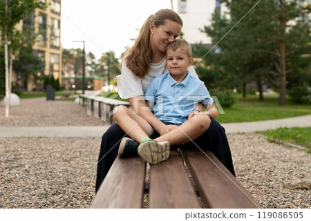 A mother and son share a joyful moment on a bench in a sunny park, highlighting their warm and 119086505