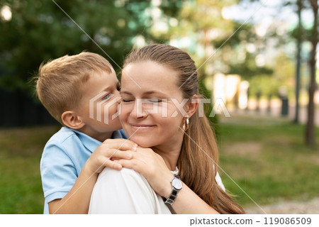 A young boy kisses his mother on the cheek as they stand in a park on a sunny day A young boy kisses his mother on the cheek as they stand in a park on a sunny day 119086509