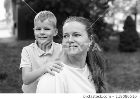 A young boy gently rests his hand on his mother's shoulder as they share a warm moment in the park 119086510