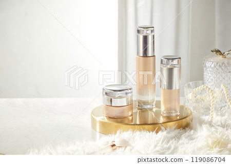 An image for promoting a beauty product features a jar and two bottles without label display on a copper tray, surrounded by a fur rug, and the glass bottle has pearl string. An image for promoting a beauty product features a jar and two bottles without label display on a copper tray, surrounded by a fur rug, and the glass bottle has pearl string. 119086704