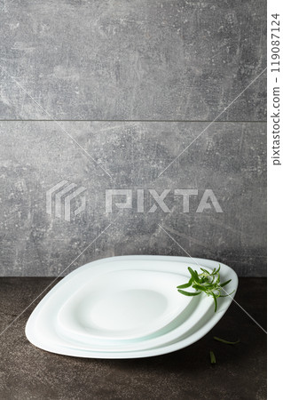 Empty white plates with rosemary on a grey stone background. 119087124