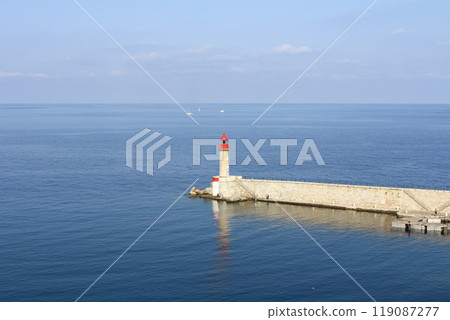 A calm seaside scene with a red lighthouse standing on the edge of a pier in Corsica, France A calm seaside scene with a red lighthouse standing on the edge of a pier in Corsica, France 119087277