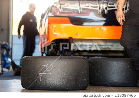 Racing slick tyres set against Nascar Whelen euro series racing sportscar vehicle Motorsport Arena garage box race track pit paddock hanged hydraulic  jack lift. European motor auto sport competition 119087460