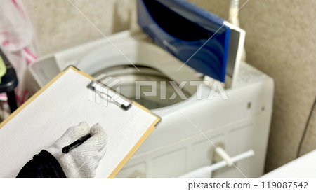A man wearing gloves holding a clipboard assessing an open washing machine A man wearing gloves holding a clipboard assessing an open washing machine 119087542