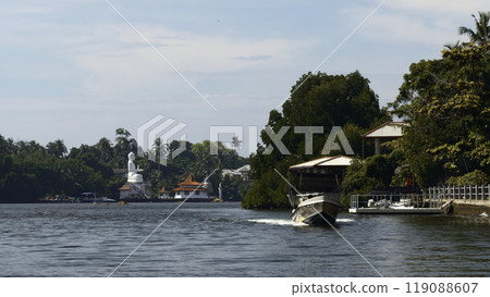 Beautiful river walk with tropical village. Action. River boats floating among jungles and settlements. River with village and Buddha statue in jungle on sunny summer day 119088607