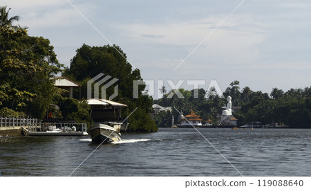 Beautiful river walk with tropical village. Action. River boats floating among jungles and settlements. River with village and Buddha statue in jungle on sunny summer day 119088640