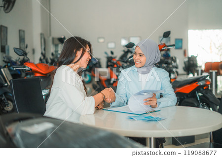 A woman and a shop assistant shake hands during a motorcycle sale agreement 119088677