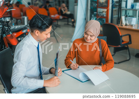 veiled woman buyer signing agreement with male salesperson at motorcycle showroom veiled woman buyer signing agreement with male salesperson at motorcycle showroom 119088695