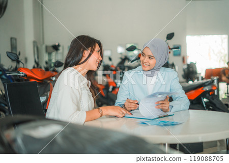 A woman and a veiled shop assistant sign a motorcycle sales agreement A woman and a veiled shop assistant sign a motorcycle sales agreement 119088705