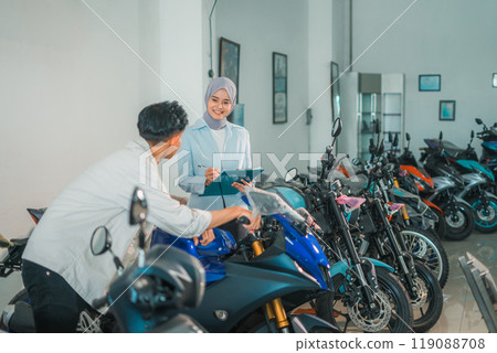 saleswoman wearing a hijab with a male customer looking at a motorcycle 119088708