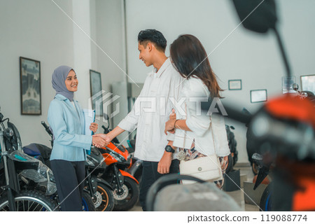 a veiled saleswoman shaking hands with a buyer at a vehicle showroom 119088774