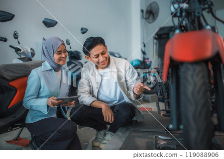 Asian man and veiled saleswoman with a tablet checking out a new motorcycle 119088906