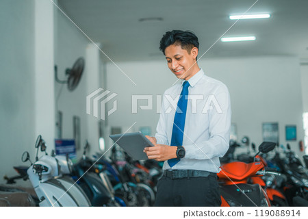 Asian man sales manager using a tablet in a motorcycle showroom Asian man sales manager using a tablet in a motorcycle showroom 119088914