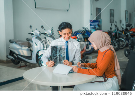 motorcycle sales man serves a veiled female customer while sitting motorcycle sales man serves a veiled female customer while sitting 119088946
