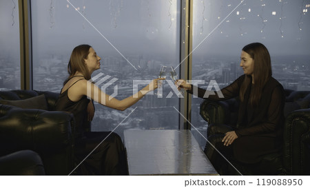 Attractive women clink glasses and drink champagne in restaurant. Media. Beautiful young women relax in champagne restaurant. Friends meet and celebrate with champagne in restaurant 119088950