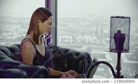 Beautiful young woman with laptop and hookah. Media. Business woman is working on laptop while relaxing in hookah bar. Woman is working on laptop in restaurant with hookah Beautiful young woman with laptop and hookah. Media. Business woman is working on laptop while relaxing in hookah bar. Woman is working on laptop in restaurant with hookah 119089069