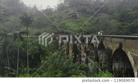 Beautiful landscape with couple walking on bridge in jungle. Action. Fabulous couple walks on stone bridge in jungle. Picturesque tropical landscape with bridge and couple in love in jungle 119089070