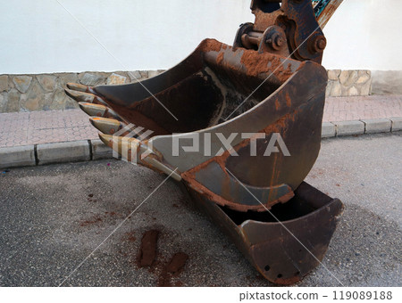 Close-up view of an excavator bucket showing details of rust and wear in a construction area during daylight 119089188