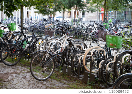 A crowded urban bicycle parking area showcasing eco-friendly transportation in a city. Represents sustainability, urban biking culture, and minimalist lifestyle trends with greenery in the background. A crowded urban bicycle parking area showcasing eco-friendly transportation in a city. Represents sustainability, urban biking culture, and minimalist lifestyle trends with greenery in the background. 119089432