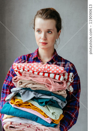 happy young European woman holds stack of folded clothes for hygienic washing at home.  119090613