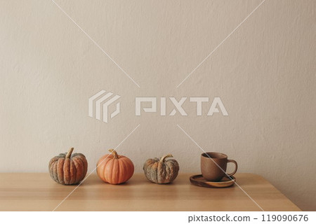 Row of little orange, white pumpkins sitting on top of wooden table. Cup of tea, coffee. Halloween autumn home decor. Thankfgiving holiday still life. Beige wall background, empty copy space. 119090676