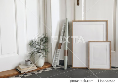 Festive Christmas indoor decor. Set of blank vertical wooden picture frames mockups, grey tiled floor. Pine tree branches in vase gift wrapping papers. White hall background. Empty artistic templates. 119090682