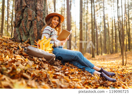 Stylish woman reading a book in the autumn park. Relaxation, enjoying, solitude with nature. 119090725
