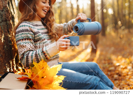 Cute young woman drinks hot drink from thermos and enjoys nature. Autumn landscape. relax concept. 119090727