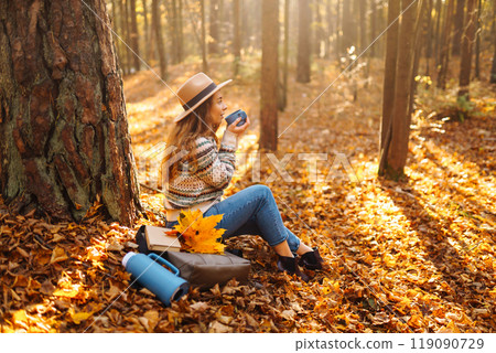 Cute young woman drinks hot drink from thermos and enjoys nature. Autumn landscape. relax concept. 119090729