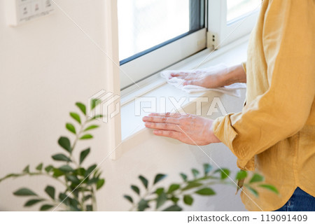 A middle-aged woman wiping and cleaning the window frames of an apartment A middle-aged woman wiping and cleaning the window frames of an apartment 119091409