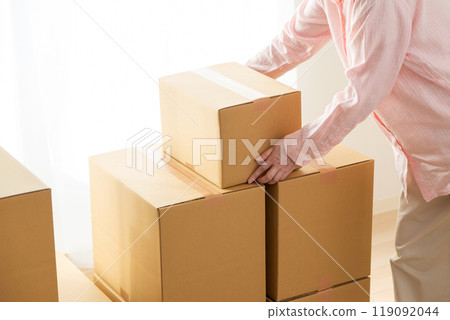 A middle-aged woman carrying many cardboard boxes containing moving luggage into a room 119092044